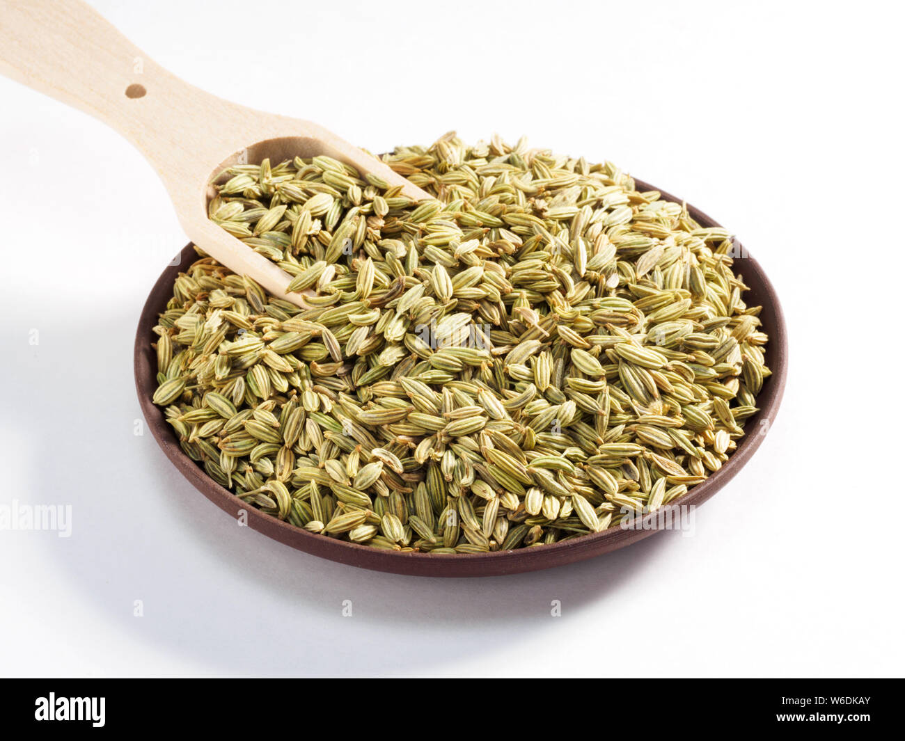 Fennel seeds (Foeniculum vulgare) in a clay plate with scoop on a white