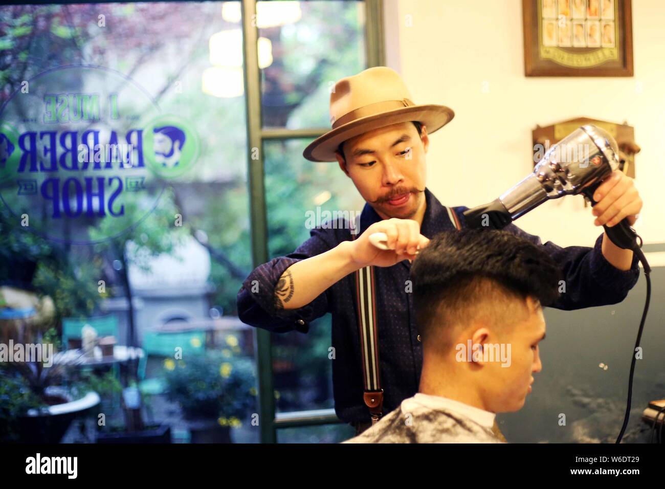 The owner of a Shanghai-based barbershop called BarberShop focusing only on men's vintage-style haircuts arranges a retro hairstyle for a customer in Stock Photo