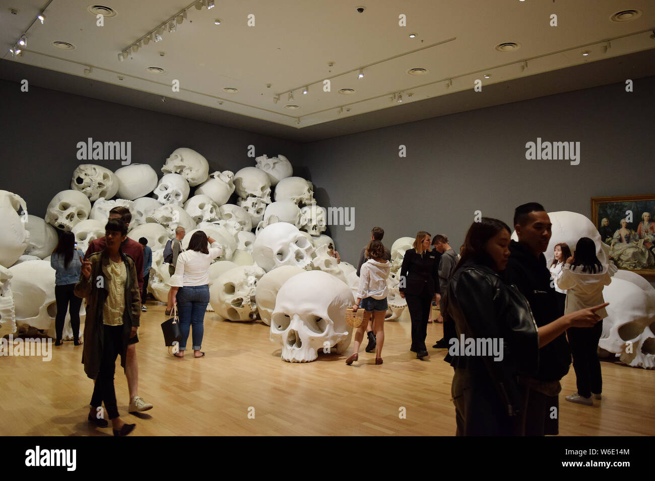 Visitors view 'Mass', an artwork of 100 larger-than-life skulls by Australian sculptor Ron Mueck, on display during the NGV Triennial art exhibition a Stock Photo