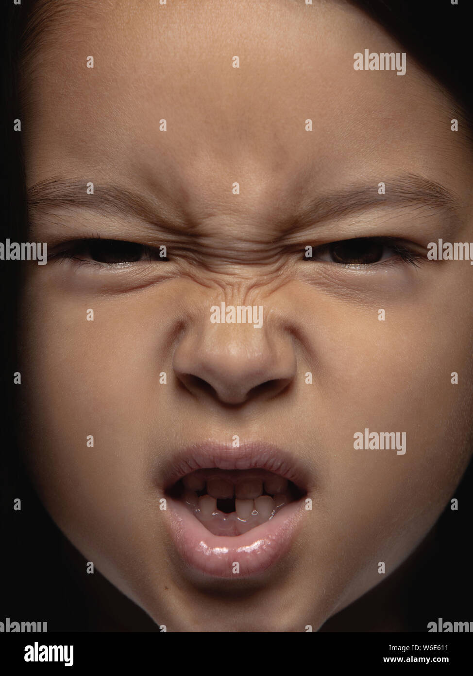 Close up portrait of little and emotional asian girl. Highly detail photoshot of female model with well-kept skin and bright facial expression. Concept of human emotions. Looks angry. Stock Photo