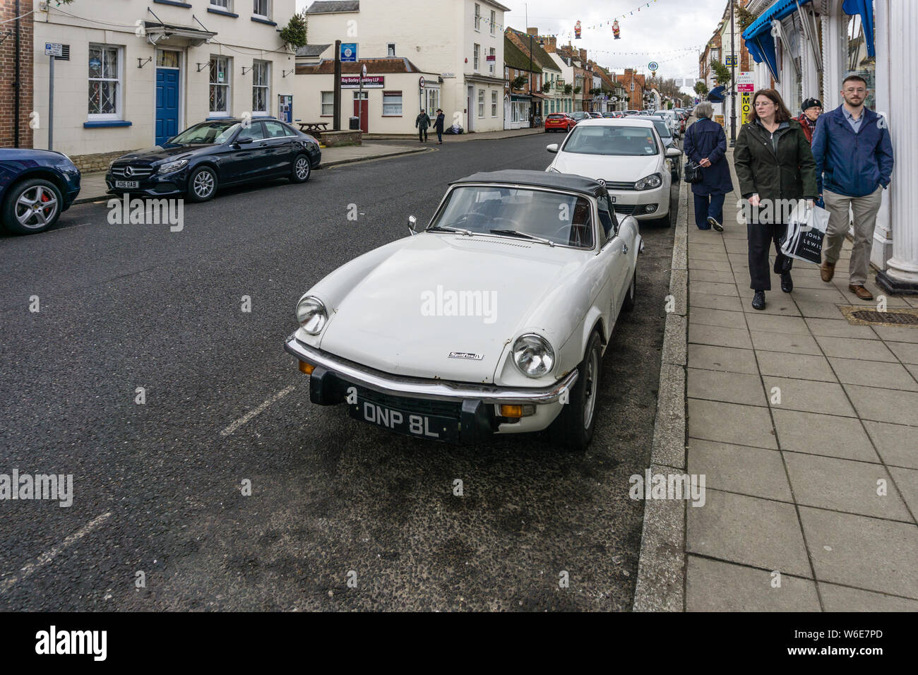 A woman shopper throws an admiring glance at a classic white Spitfire sports car, High Street, Stony Stratford, UK Stock Photo