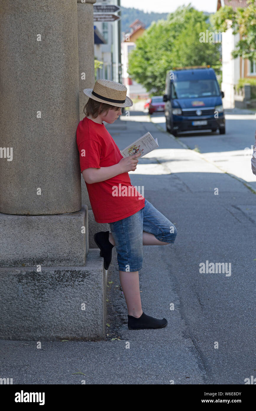 boy leaning on house wall reading a book, Zwiesel, Bayerischer Wald, Bavaria, Germany Stock Photo