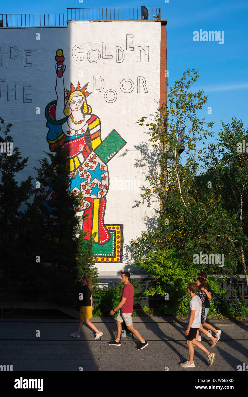 USA dark, view of people walking past a section of the painting 'I Lift My Lamp Beside the Golden Door' by Dorothy Iannone, High Line, New York. Stock Photo