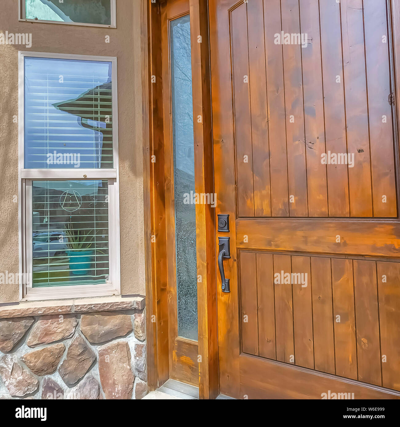 Facade of a home with shiny brown wooden front door and sidelight Stock