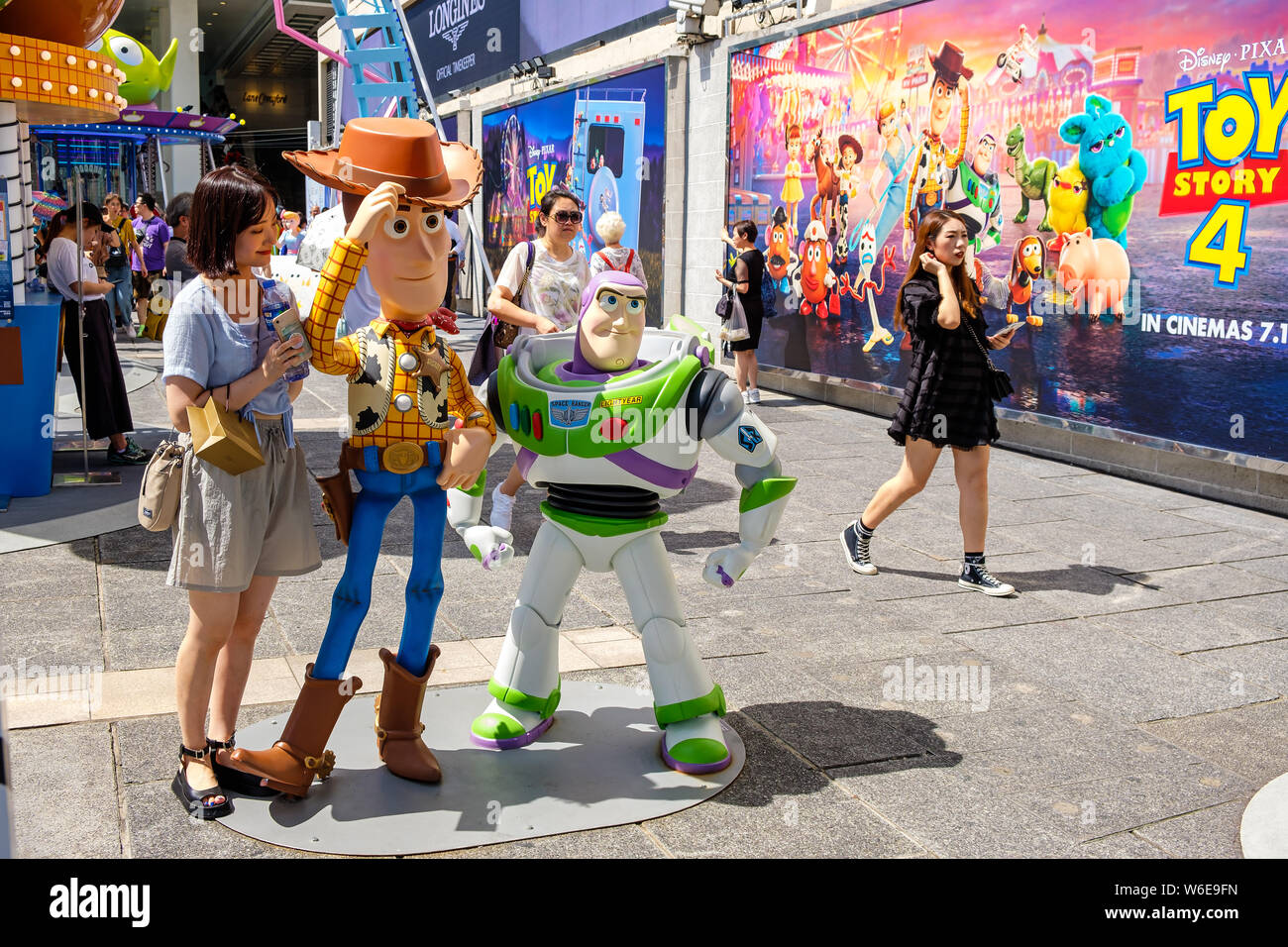 A woman posses next to replicas of Sheriff Woody and Buzz Lightyear during the Carnival.Toy Story 4 is celebrated with a themed carnival of different games and challenges at Hong Kong Harbour City. Stock Photo
