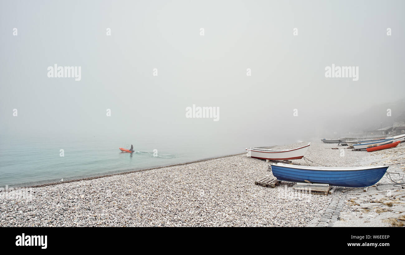 Blue and red fishing boats on a rocky pebble beach in the early morning ...