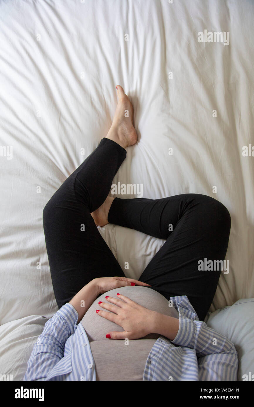 A young pregnant woman resting at home sitting on a bed. Expectant mother Stock Photo