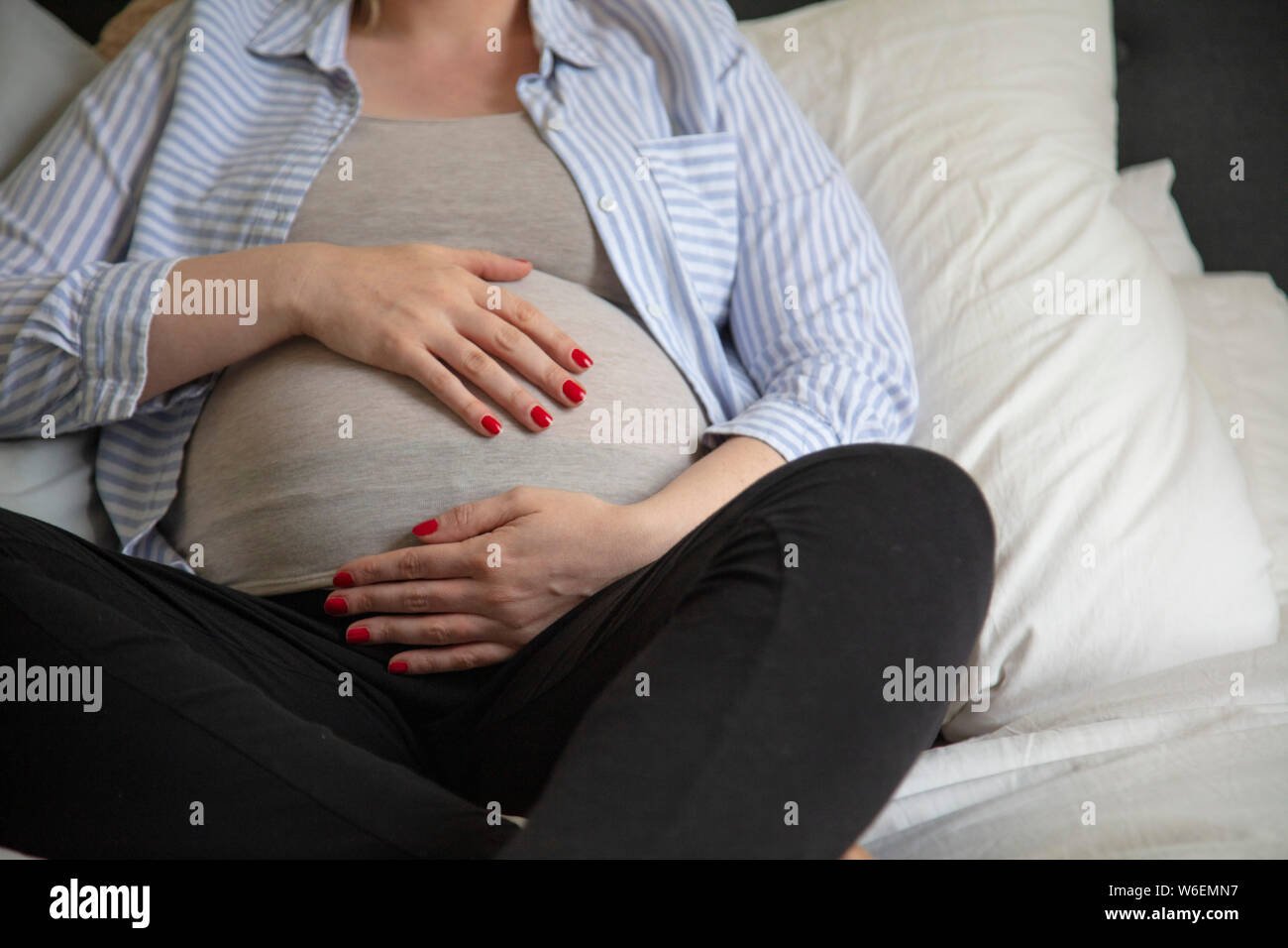 A young pregnant woman resting at home sitting on a bed. Expectant mother Stock Photo