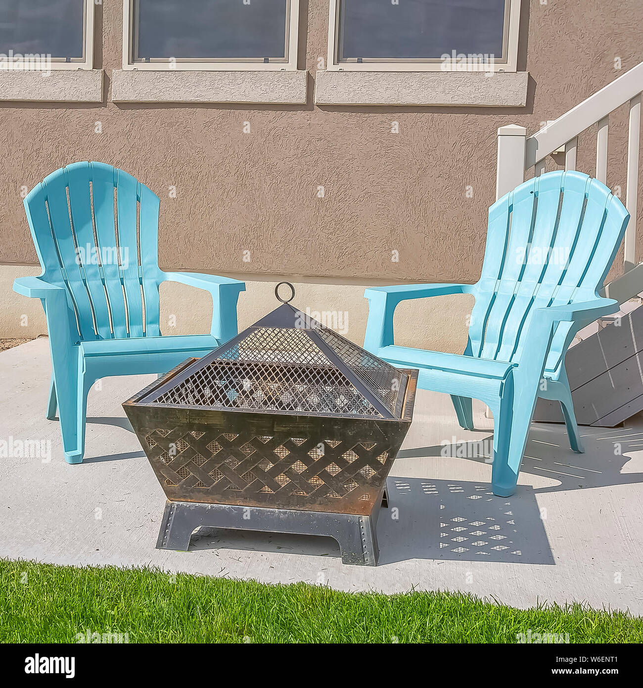 Square fire pit and blue plastic chairs on the yard of a home on a sunny day Stock Photo