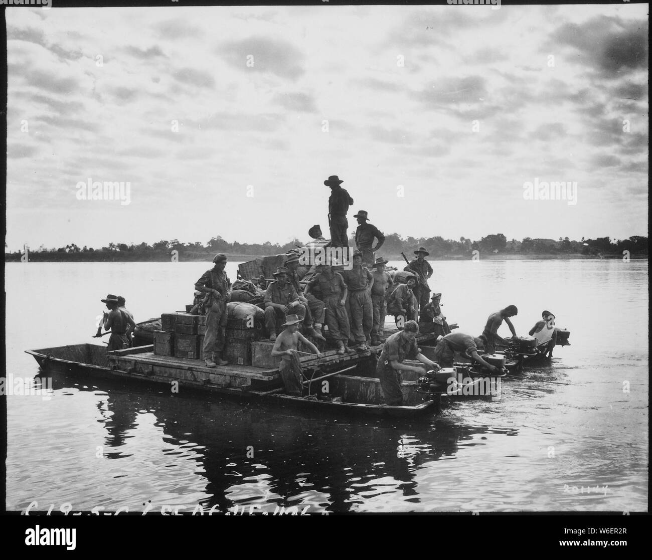 A barge, powered by outboard motors, crosses the Irrawaddy River near Tigyiang, Burma. The men, their truck and ammunition all make the crossing at once in this way.; General notes:  Use War and Conflict Number 1157 when ordering a reproduction or requesting information about this image. Stock Photo