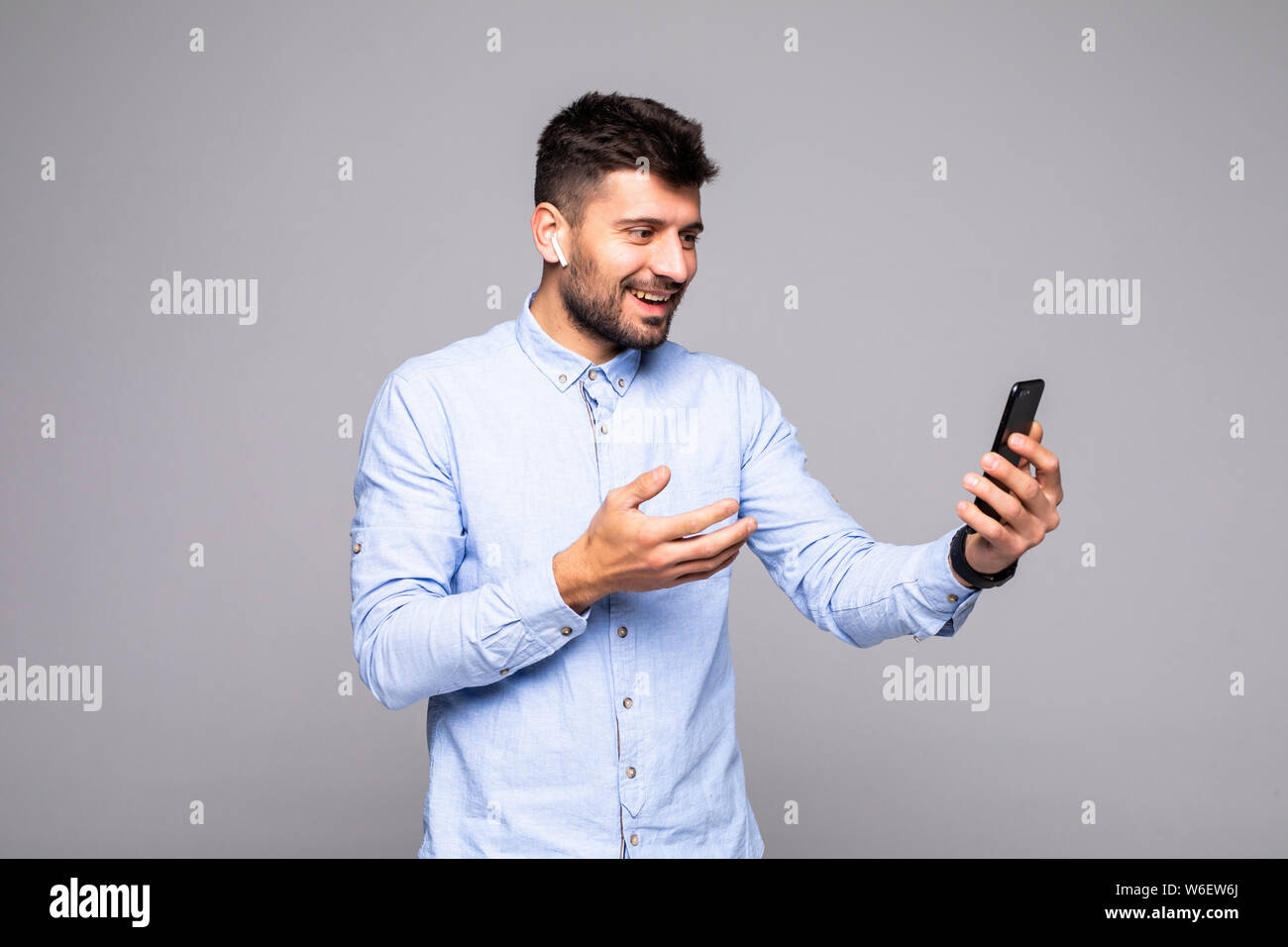 Happy smiling man watching funny video on mobile phone gadget while  standing isolated in studio against wall with copy space for promotional  content Stock Photo - Alamy