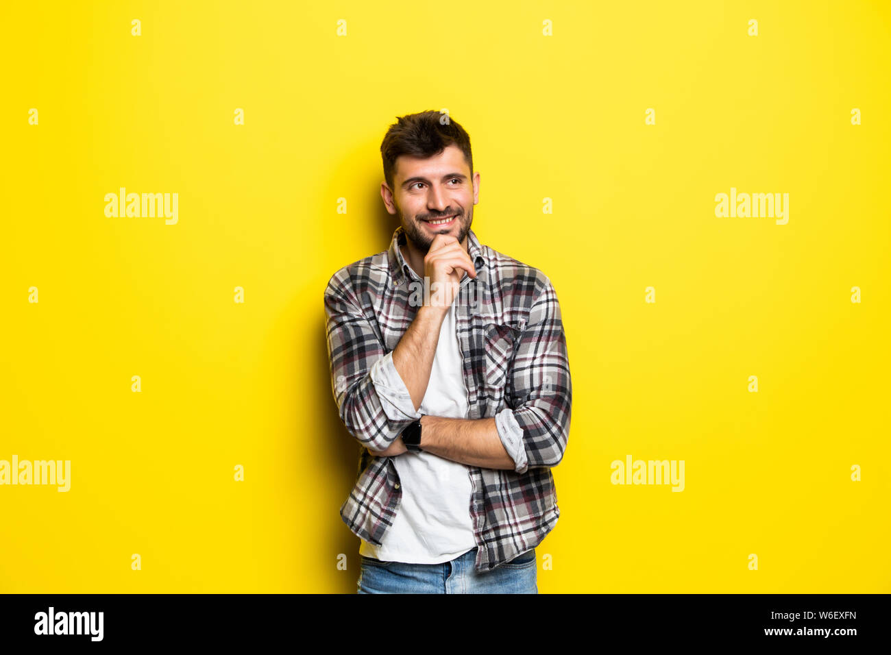 Close up portrait of thoughtful man who looks away touching his chin and weighs the pluses and minuses of the offer isolated on bright yellow backgrou Stock Photo