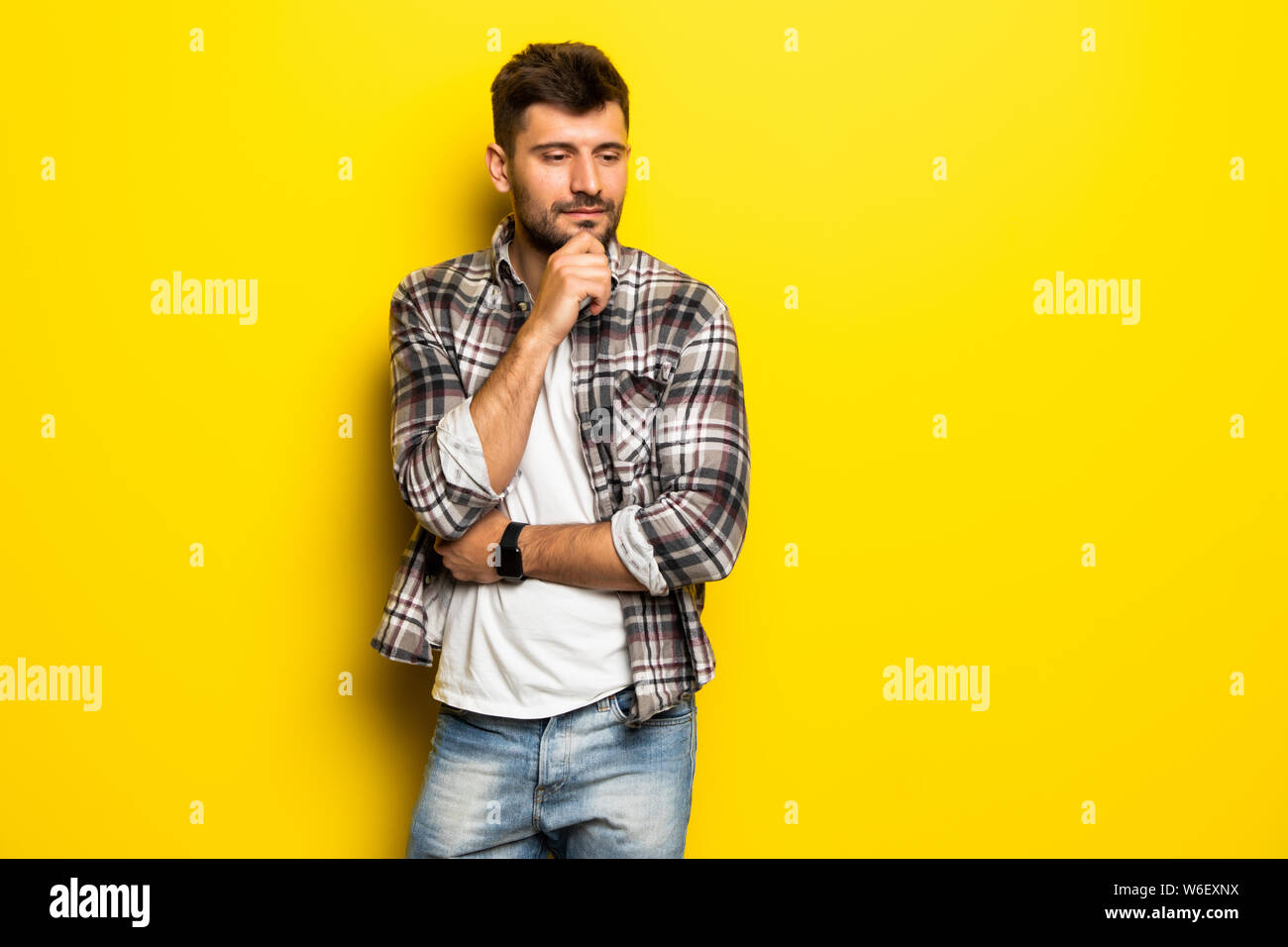 Close up portrait of thoughtful man who looks away touching his chin and weighs the pluses and minuses of the offer isolated on bright yellow backgrou Stock Photo