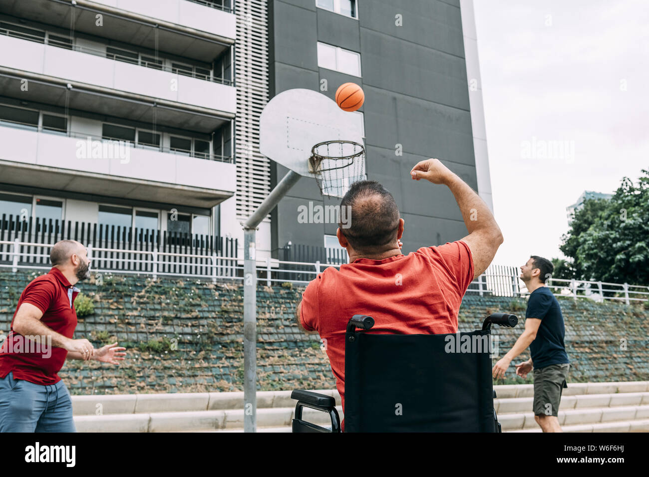 joyful disabled man in wheelchair throwing the ball to basket with two