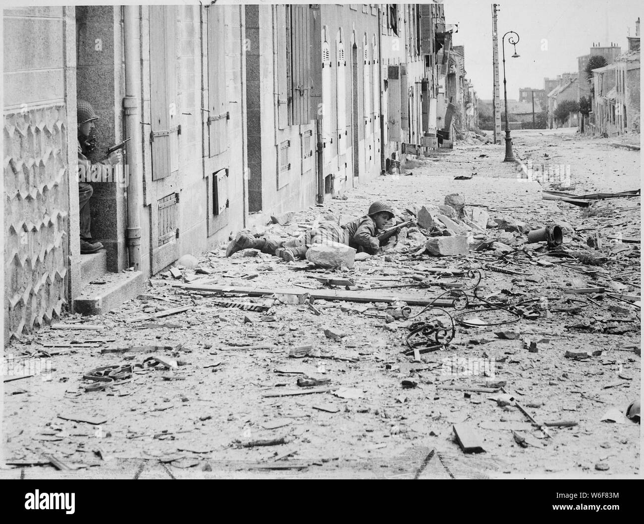 Americans take shelter during mop-up of Brest. Crouching behind a pile of rubble, a U.S. soldier watches for German snipers in the streets of Brest, while a companion covers him from behind a doorway. International News Photos.; General notes:  Use War and Conflict Number 1054 when ordering a reproduction or requesting information about this image. Stock Photo