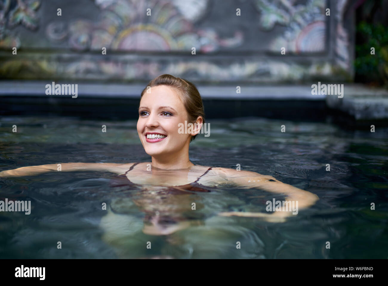 Young smiling woman swimming outdoors in exotic spa pool of luxurious hotel during tropical vacation in Bali Stock Photo