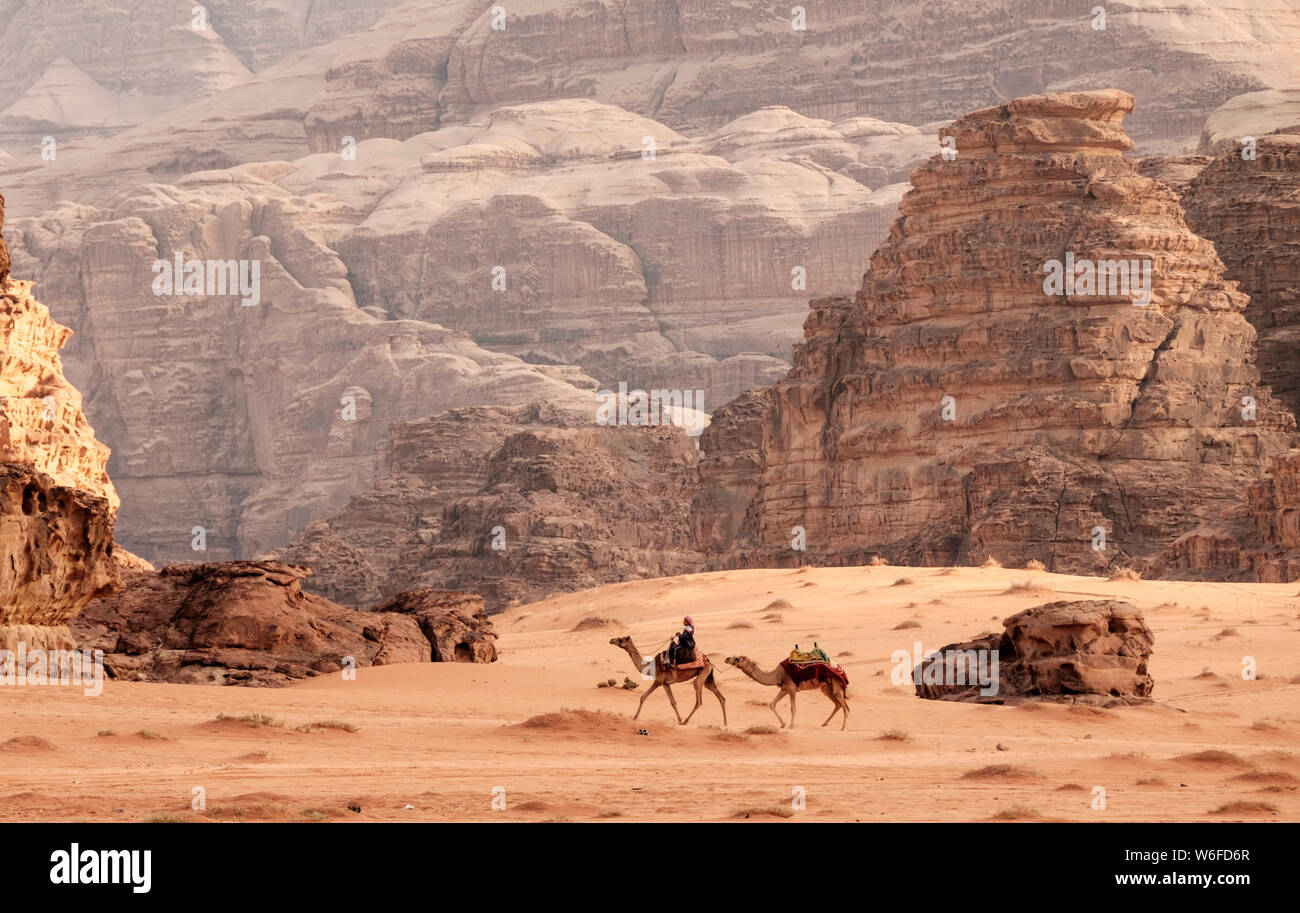 A Zalabia Bedouin camel rider leads a second camel past the impressive rock landscape of the Wadi Rum desert in Jordan. Stock Photo