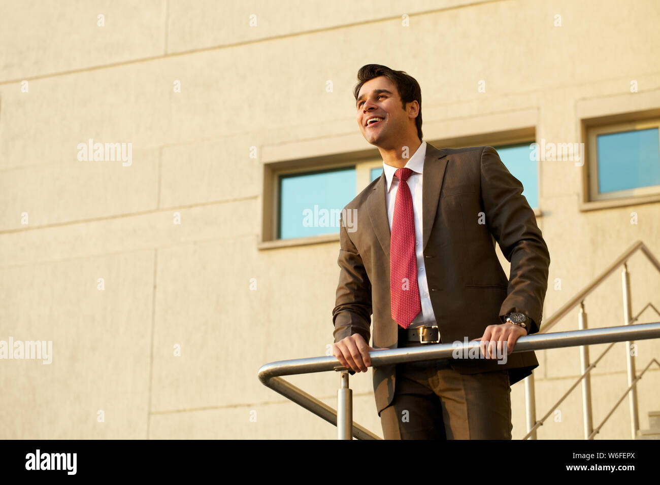 Businessman leaning against railing and smiling Stock Photo - Alamy