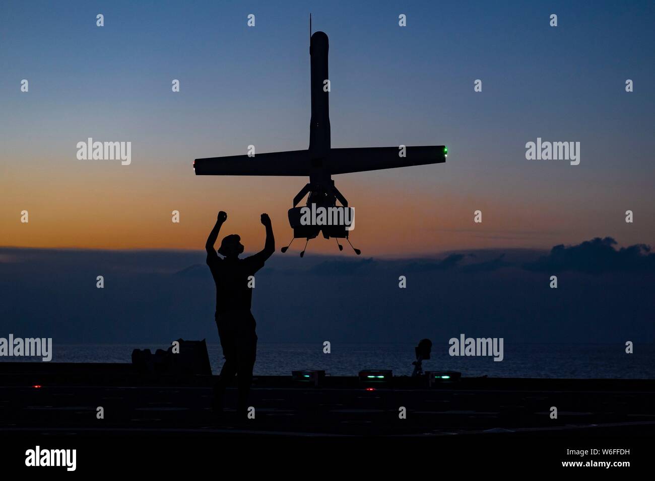 A U.S. Navy VBAT vertical take-off and landing unmanned aerial system drone prepares to land on the flight deck of the Military Sealift Command expeditionary fast transport vessel USNS Spearhead at sunset July 24, 2019 in the Atlantic Ocean off the coast of Florida. The VBAT UAS provides improved detection and monitoring to support counter-narcotics missions in the Caribbean and Eastern Pacific. Stock Photo