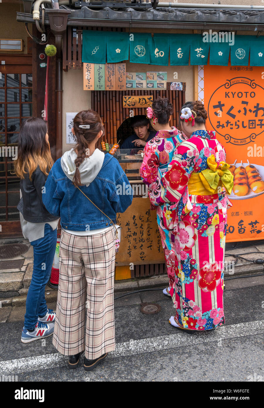 Young women wearing traditional kimonos buying dumplings from a Dango stall in the historic Gion district, Kyoto, Japan Stock Photo