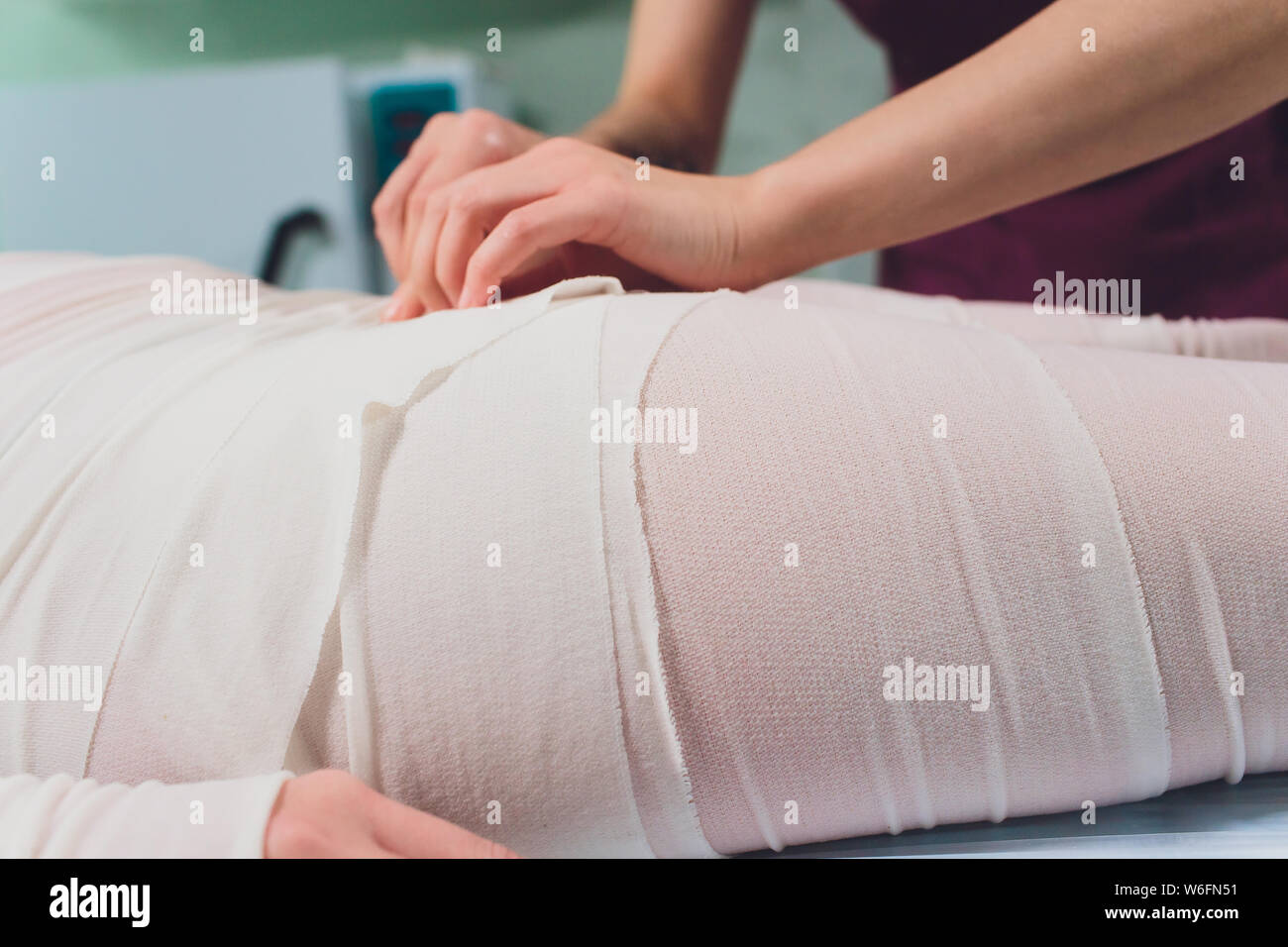 The cosmetologist wraps the leg of the customer. Anticellulite