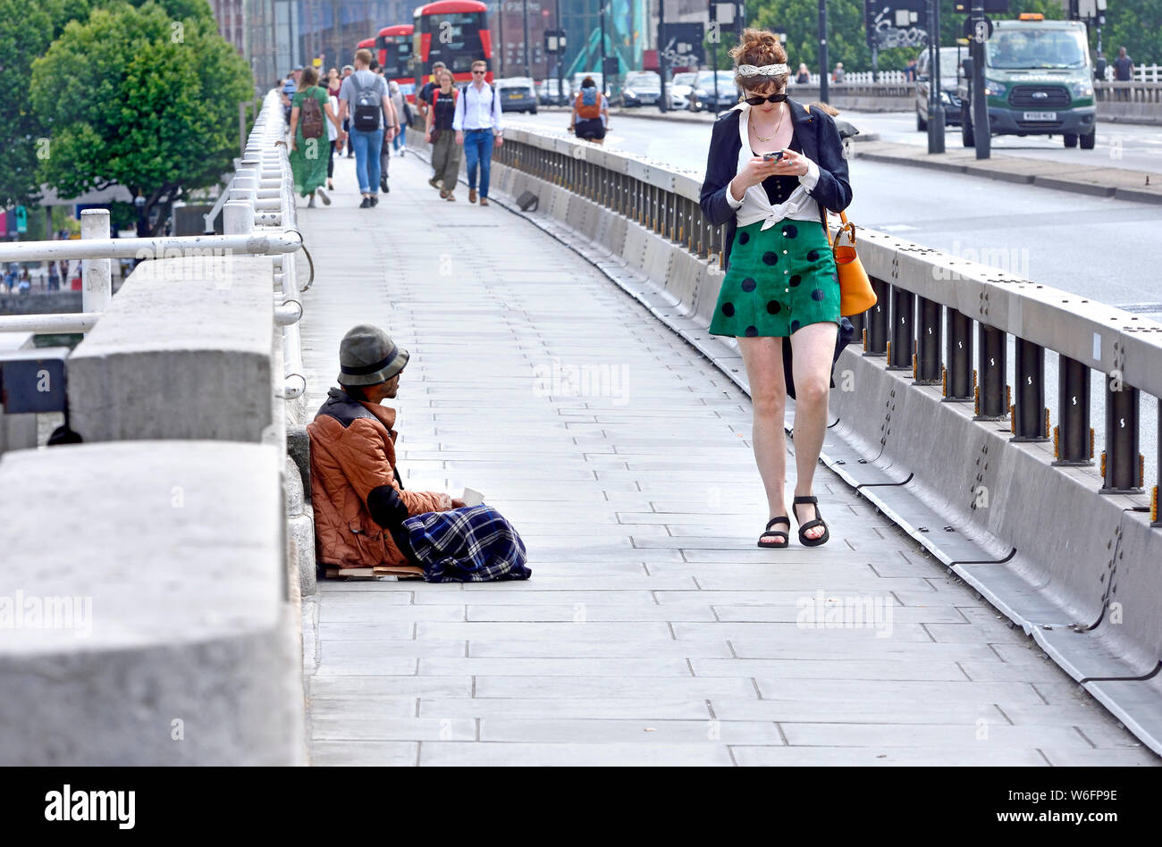 London, England, UK. Homeless man begging on Waterloo Bridge, young woman walking past Stock Photo