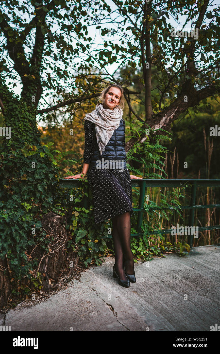 Pretty young woman wearing a dress and standing on bridge surrounded by ...