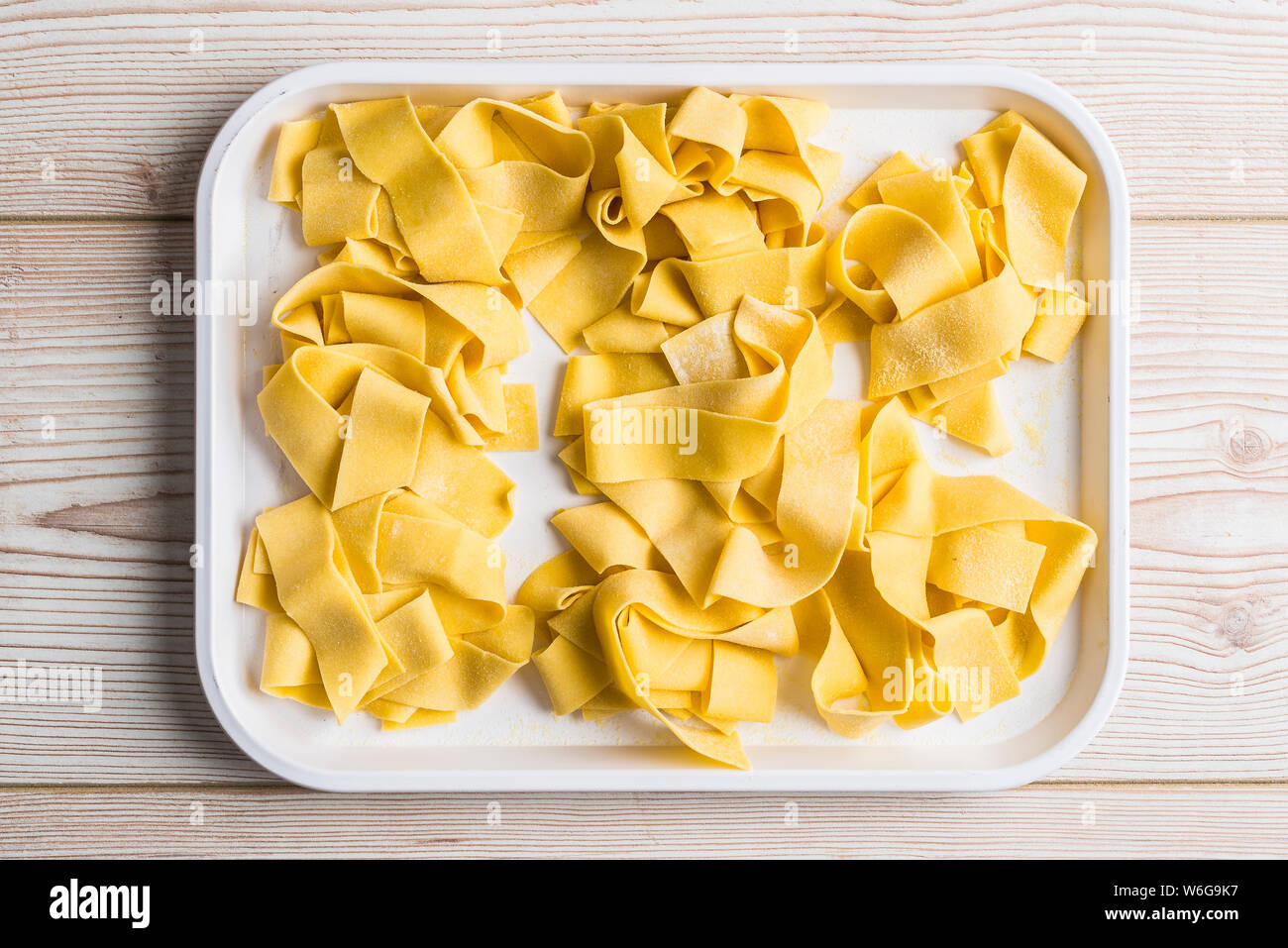 Fresh pappardelle pasta on a white tray sat on a wooden table. Stock Photo