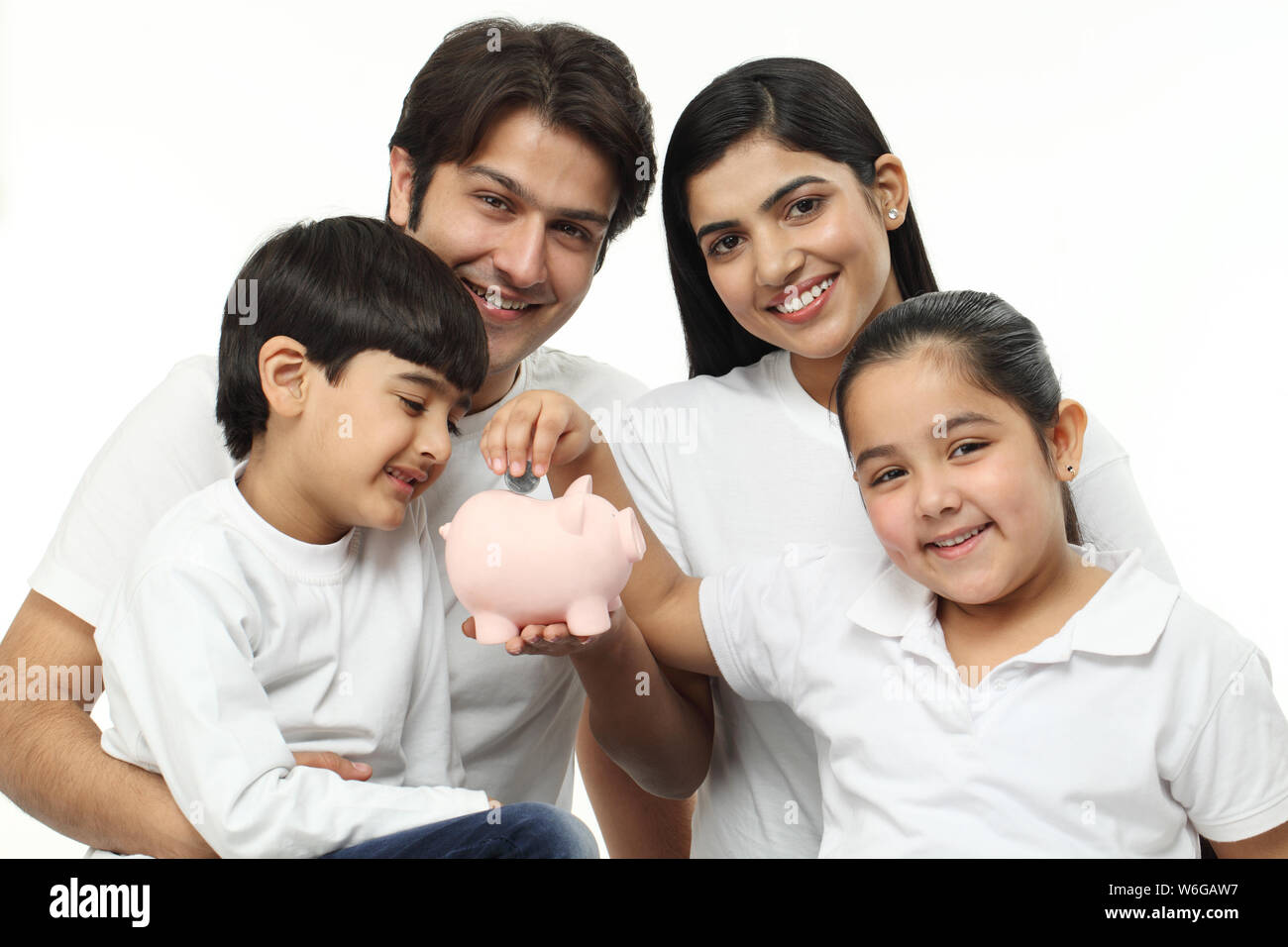 Girl putting coin into a piggy bank with their family Stock Photo - Alamy