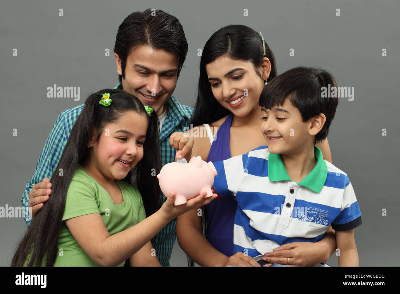 Boy putting coin into a piggy bank with their family Stock Photo - Alamy
