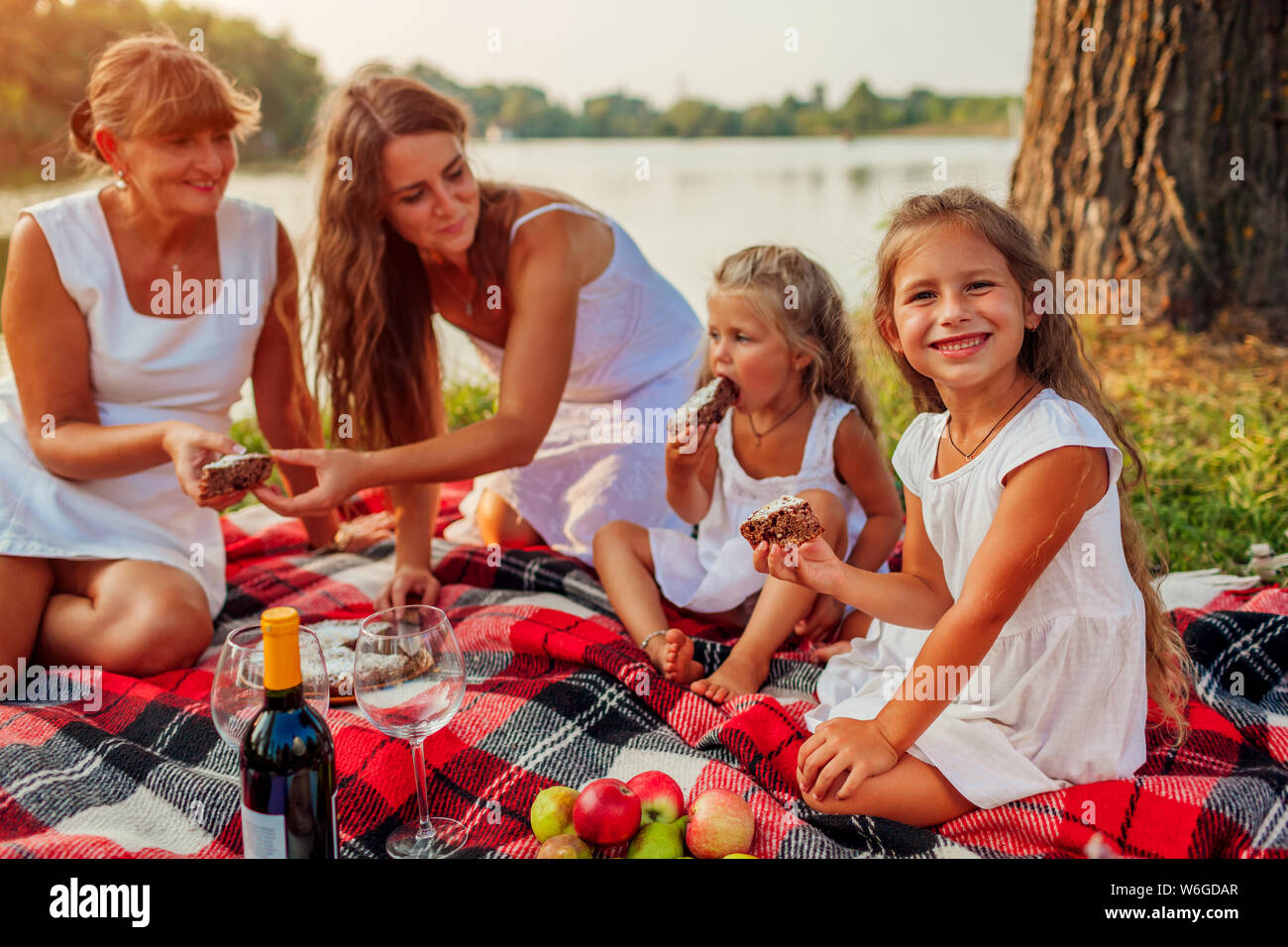 Family having picnic by summer river at sunset. Mother, grandmother and