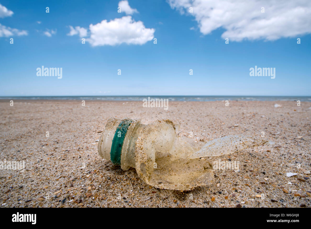 Old partly broken down plastic bottle, non-biodegradable waste washed ashore on sandy beach along the North Sea coast Stock Photo