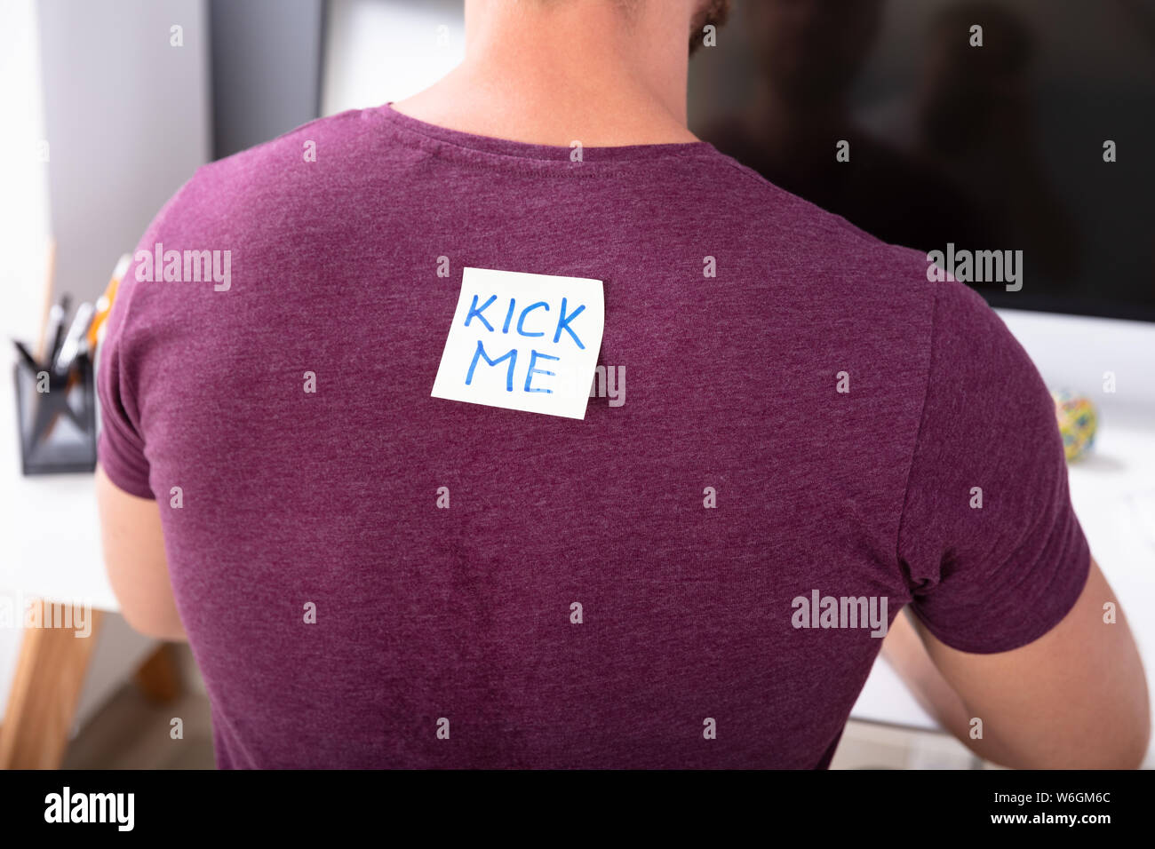 Rear View Of Man Working In Office With Kick Me Text Written On Sticky Note Stock Photo