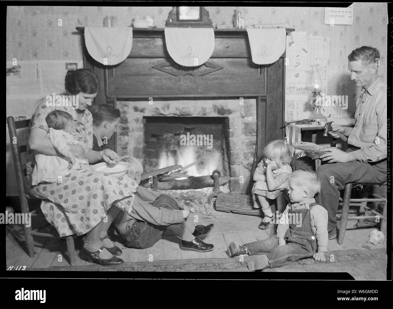 Family group of Fletcher Carden, Route #1, Andersonville, Tennessee, a night-watchman at the bunkhouses at Norris Dam. His home is on the townsite of Norris and will be moved. Carden has 12 children. He is shown here repairing shoes at the fireside. Stock Photo