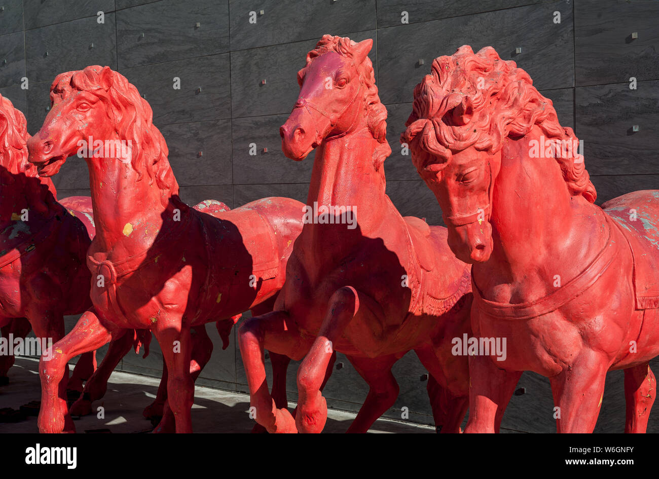 Red horses sculptures, in a row, on gray stones wall background. Stock Photo