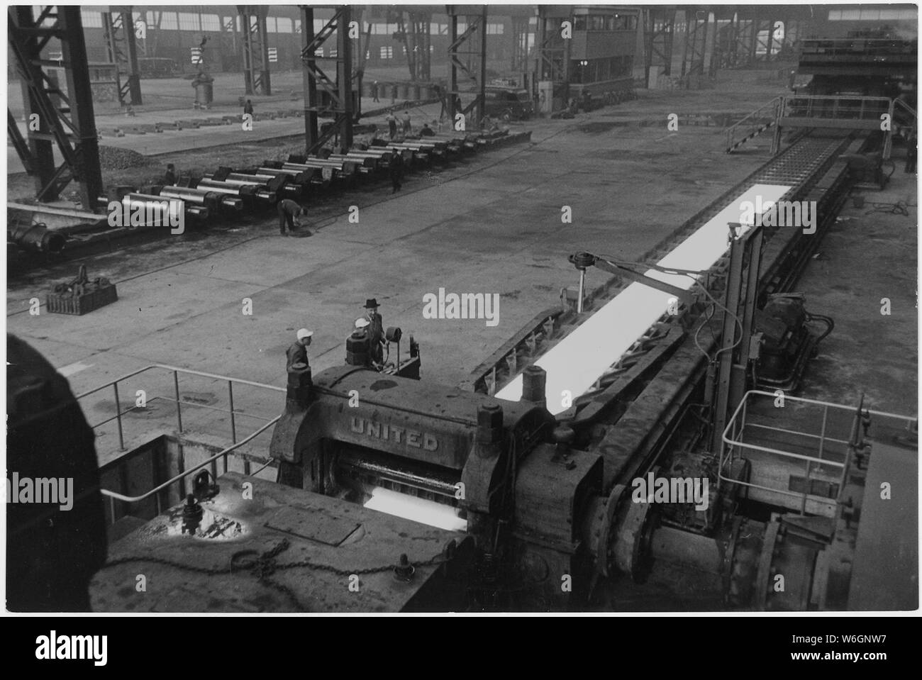 France. Note in background, ramp built over the strip for workmen to cross back and forth. On left side of the picture are extra rollers. Steel is rough on rollers, which must frequently be turned and polished to remove pit-marks, and to insure that calculations in each stage of the strip-mill are constant Stock Photo