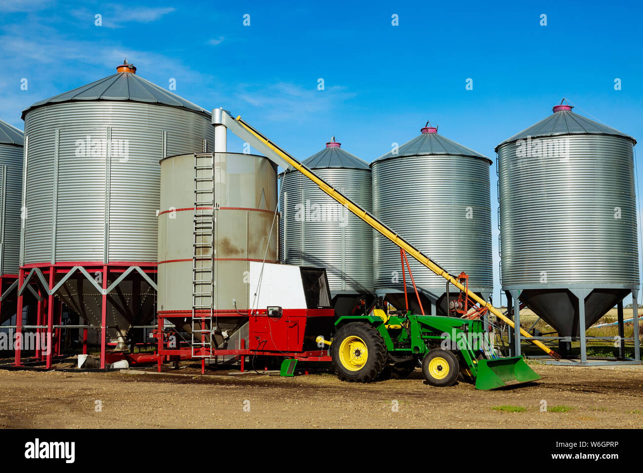 Silos in the background with a tractor and auger for loading a grain