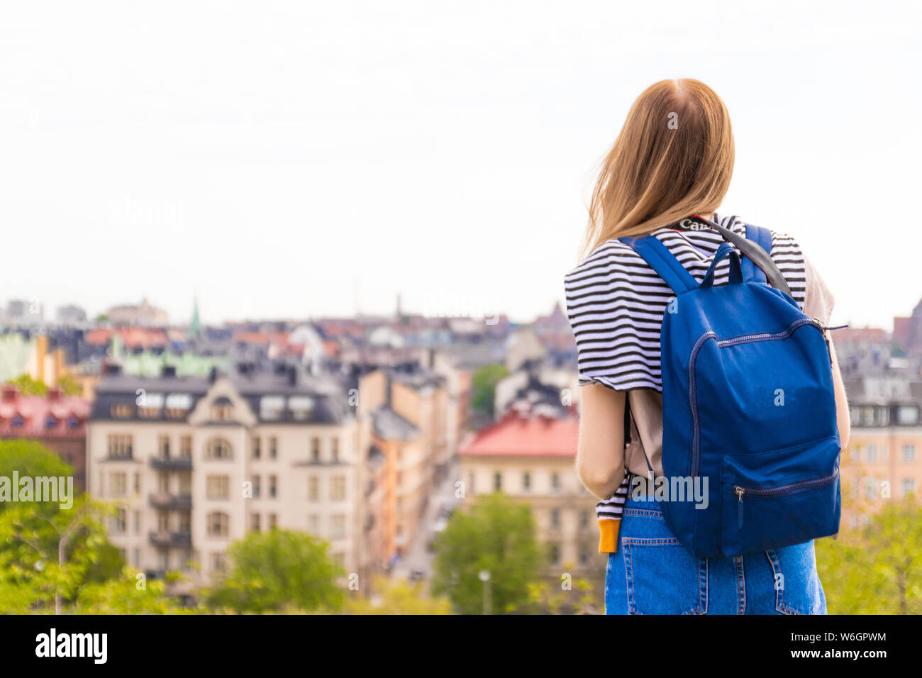 Rear view of young woman in a blue backpack looking look at the city ...
