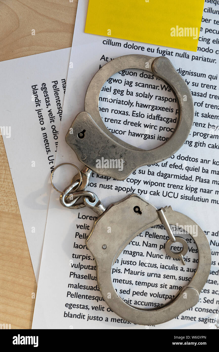Silver Handcuffs and key on document with yellow note  attached. Stock Photo. Stock Photo