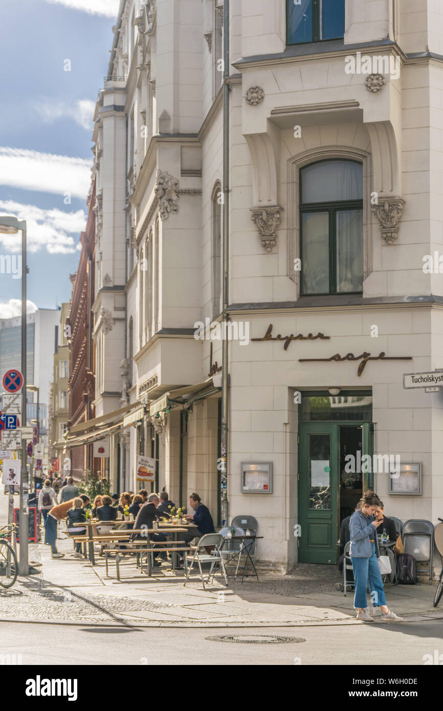 BERLIN, GERMANY - SEPTEMBER 26, 2018: Girl checks her phone in front of some buildings in the sidewalk of a busy street with people sitting in tables Stock Photo