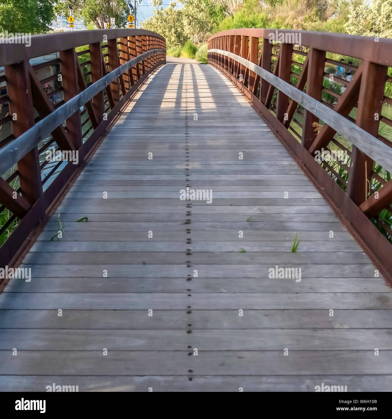 Square Bridge with wood deck and rusty metal railing over a lake with ...