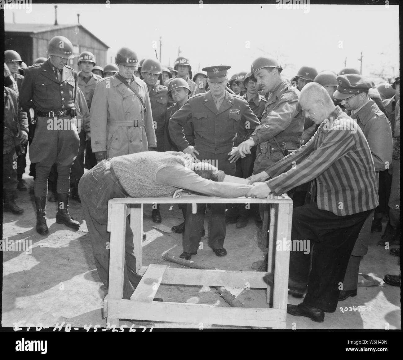 General Dwight D. Eisenhower watches grimly while occupants of a German concentration camp at Gotha demonstrate how they were tortured by the Nazi sadists operating the camp. Generals Bradley and Patton are at his right. Germany; Scope and content:  On pages 275 and 276 of General Patton's book, War As I Knew It, Patton describes the events leading up to and including the one depicted in this photo.  He states that he, Eisenhower and Bradley learned later, that the person in the striped shirt, demonstrating the torture, was actually one of the camp's executioners.  Patton notes that this man w Stock Photo