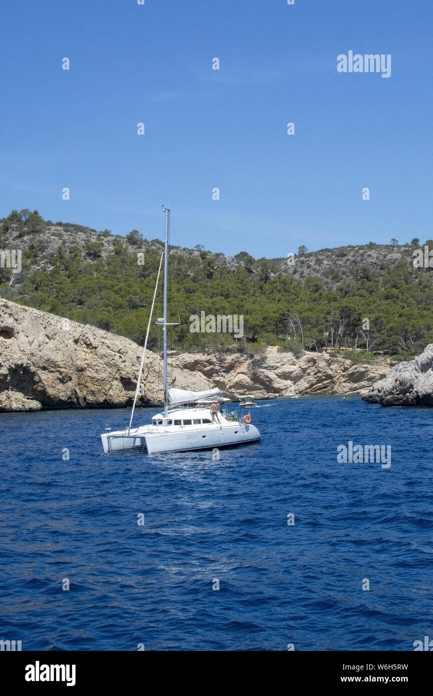 MALLORCA, SPAIN - JUNE 23, 2019: White camaran with people anchored near rocky coast on a sunny day on June 23, 2019 in Mallorca, Spain. Stock Photo