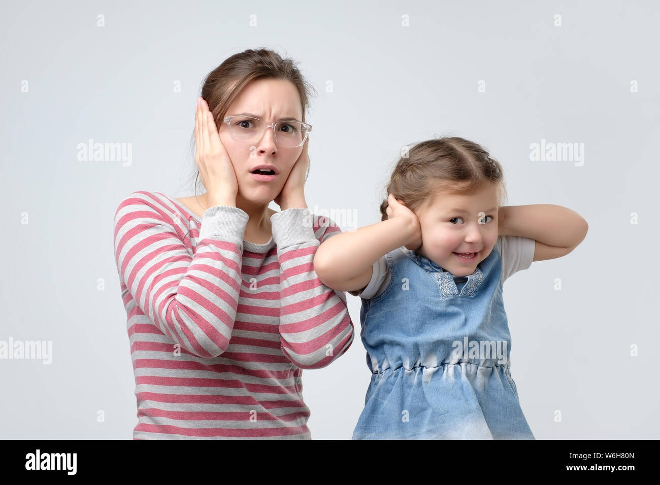 woman and her little daughter cover ears with hands. Avoid loud noise. Stock Photo