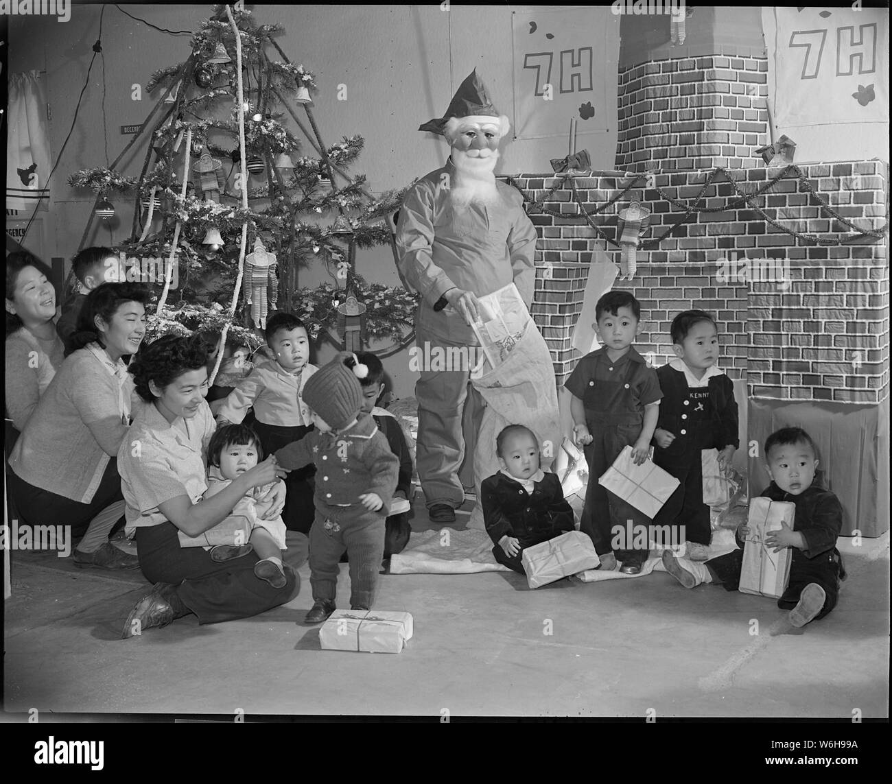 Granada Relocation Center, Amache, Colorado. Chief Steward Matsumoto of Block 7-H at the Granada Re . . .; Scope and content:  The full caption for this photograph reads: Granada Relocation Center, Amache, Colorado. Chief Steward Matsumoto of Block 7-H at the Granada Relocation Center dons some red pajamas and a Santa Claus mask to make Christmas real for the children whose barracks room homes have no Christmas trees. they are the children of persons of Japanese ancestry evacuated from the west coast. The gifts, provided by churches throughout the United States for the children of the ten relo Stock Photo