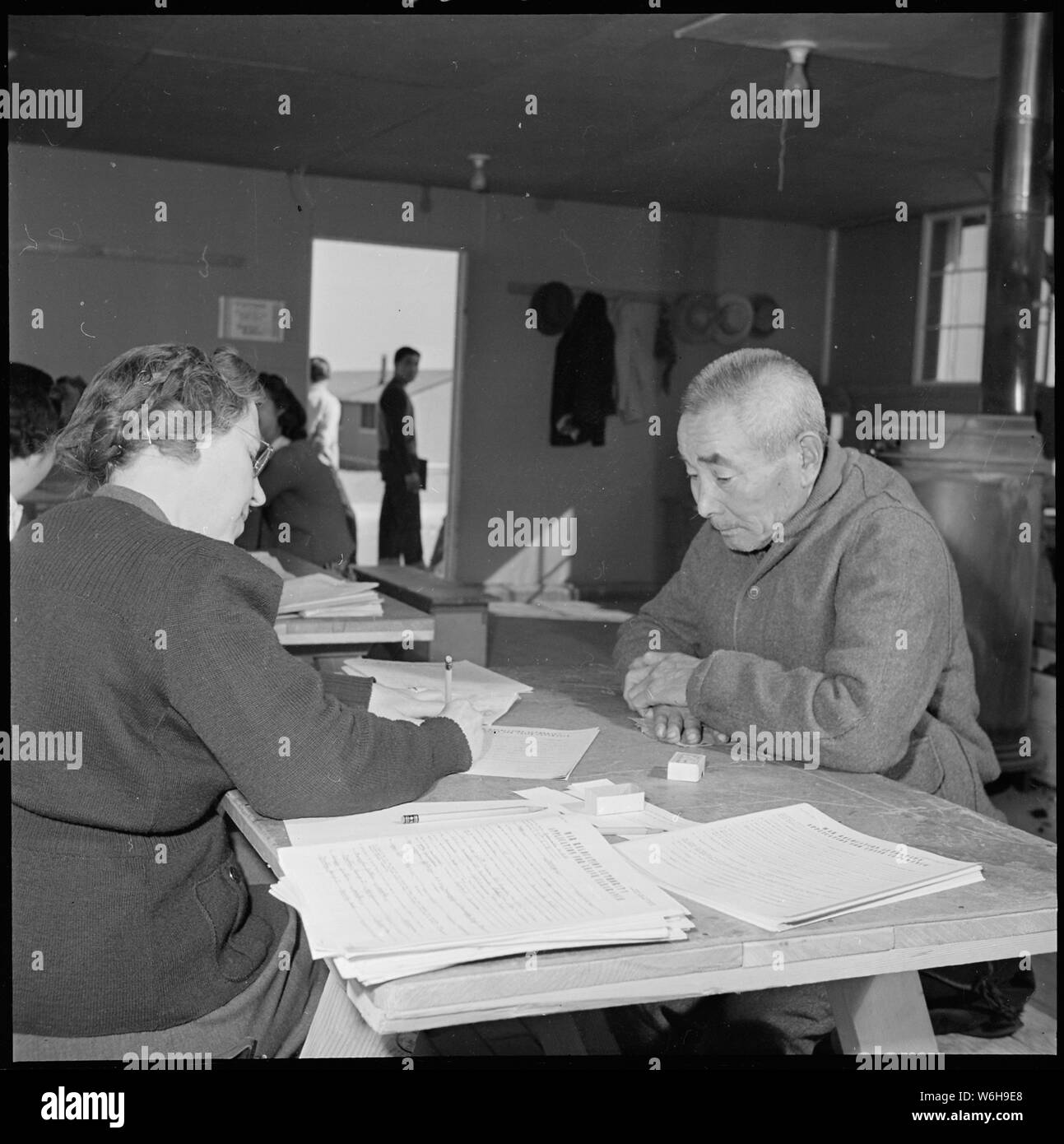 Granada Relocation Center, Amache, Colorado. Elizabeth Evans, Japanese speaking member of the Educa . . .; Scope and content:  The full caption for this photograph reads: Granada Relocation Center, Amache, Colorado. Elizabeth Evans, Japanese speaking member of the Education Department at the Granada Center, assists Shuhei Ichishima, alien Japanese of Nugata, Japan, who had resided in Yuba City, California for 21 years before evacuation to the relocation center. The general registration of all residents in relocation centers was instigated by the Army and the War Relocation Authority as the fir Stock Photo