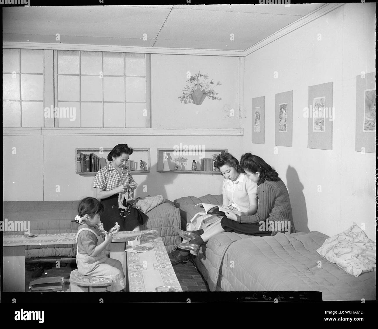 Granada Relocation Center, Amache, Colorado. Sunday afternoon and the three girls who occupy this b . . .; Scope and content:  The full caption for this photograph reads: Granada Relocation Center, Amache, Colorado. Sunday afternoon and the three girls who occupy this barracks room relax. The furniture, the book niche, flower pot and print mats are all made by the girls from scrap lumber and scrap pieces of wall board. Stock Photo