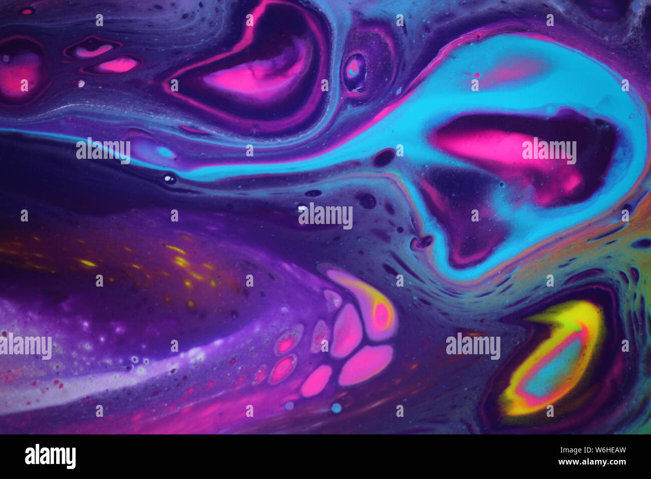 Abstract acrylic pour painting for backgrounds that features bright neon colors as well as dark purple for contrast, and has a cosmic feel. Stock Photo