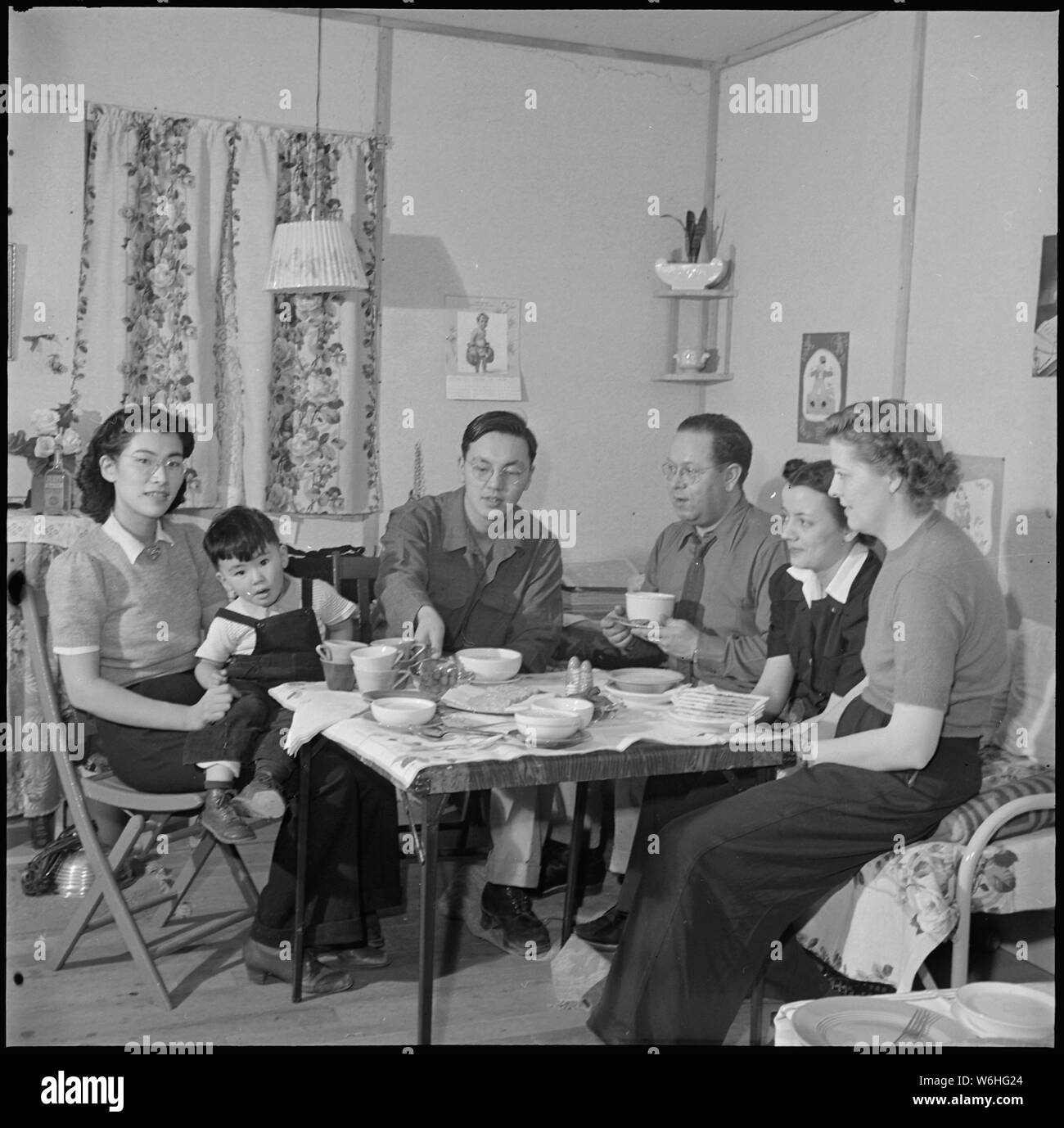 Heart Mountain Relocation Center, Heart Mountain, Wyoming. In his barracks home at Block 7 - 21, Bi . . .; Scope and content:  The full caption for this photograph reads: Heart Mountain Relocation Center, Heart Mountain, Wyoming. In his barracks home at Block 7 - 21, Bill Hosokawa and his wife Alice serves oyster stew in an evening's visit with the members of the War Relocation Authority appointed personnel. Left to right is Julona Steinheider, High School Mathematics Teacher; Margaret Jensen, Center Librarian; Vaughn Mechau, Reports Officer; Bill, his son Mike and his wife, Alice. (This appea Stock Photo