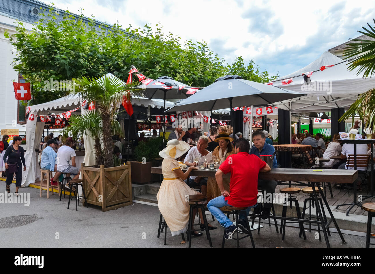 Vevey, Switzerland - Aug 1 2019: People celebrating Swiss National Day in outdoor restaurant. Celebration of the founding of the Swiss Confederacy. Independence day. Switzerland flags decoration. Stock Photo